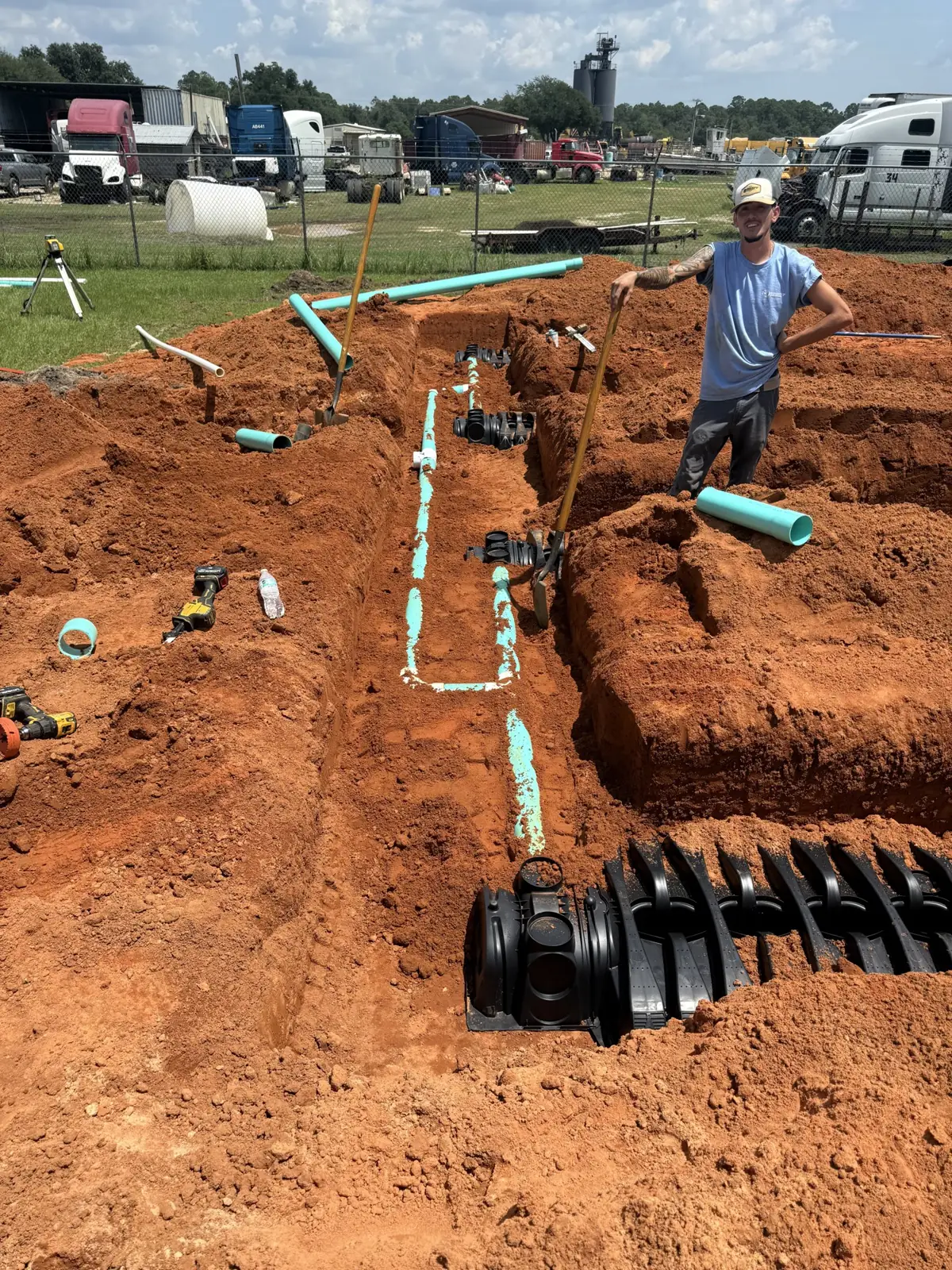 Crew member beside open trenches with teal pipe and a tank