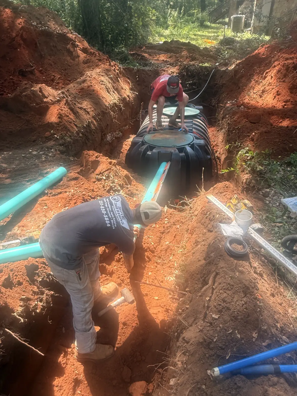 Crew setting a tank in a trench with teal pipe