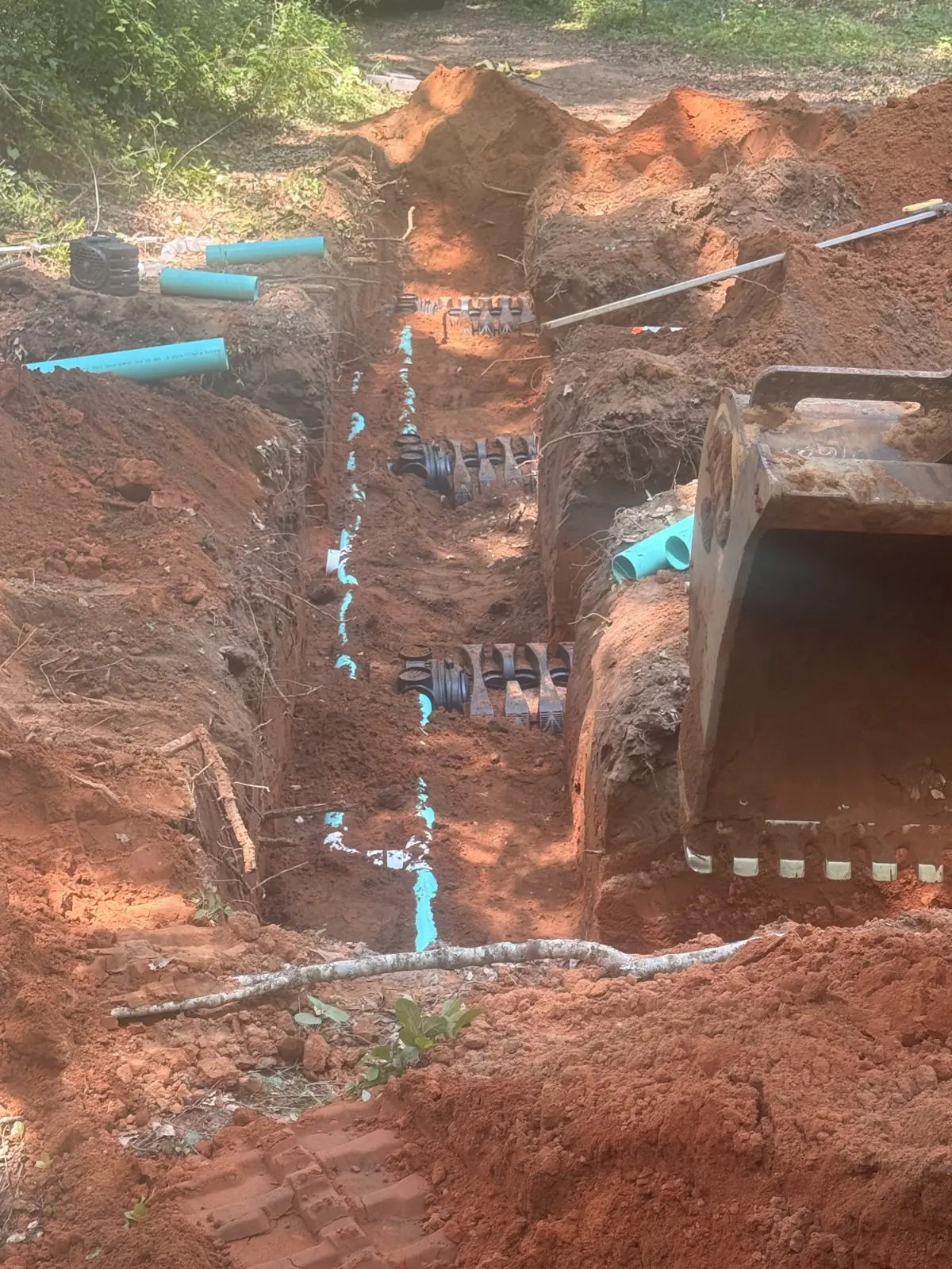 Excavator bucket beside drain field piping in a trench