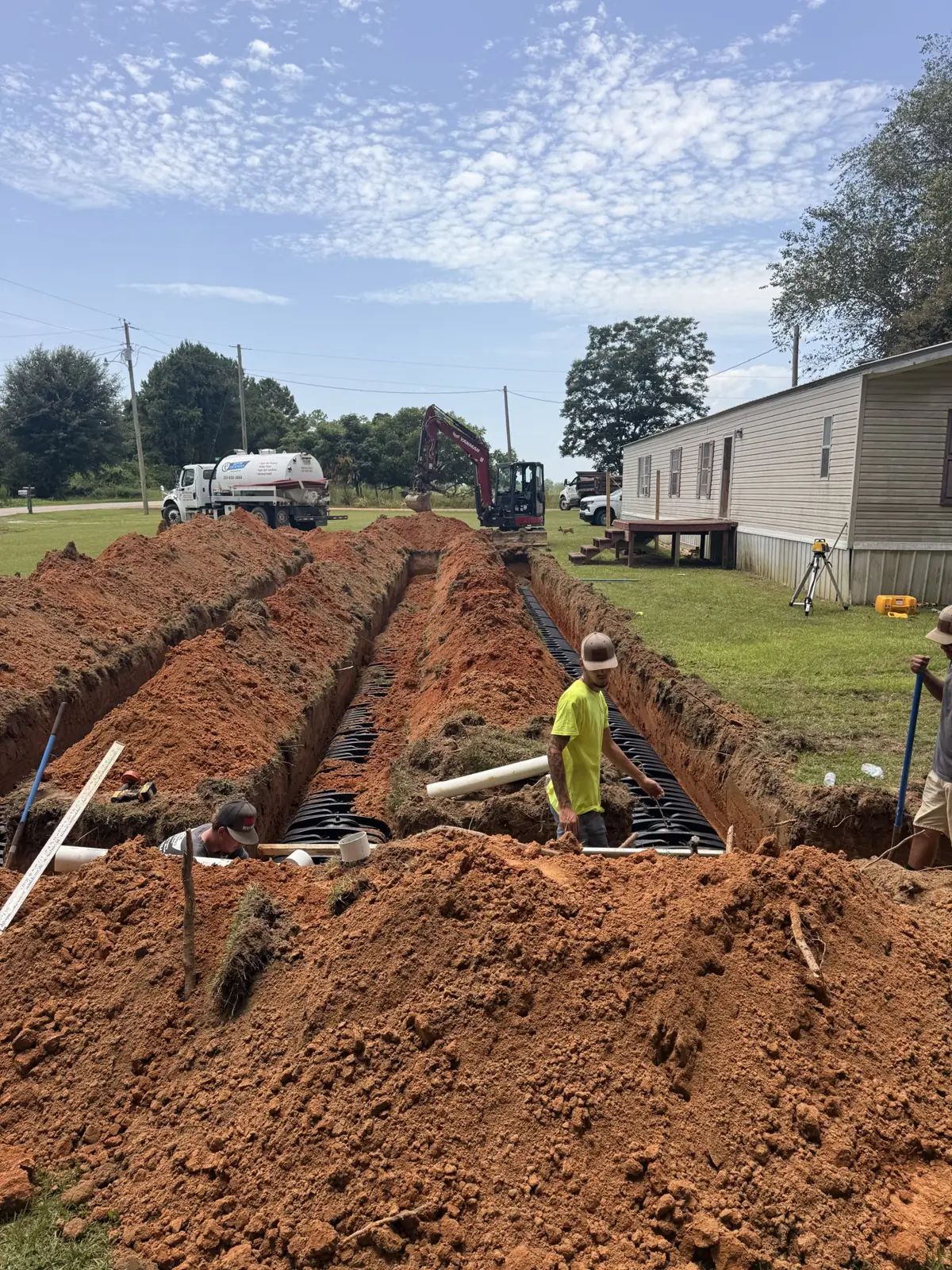 Field-line trenches cut across a lot beside a home