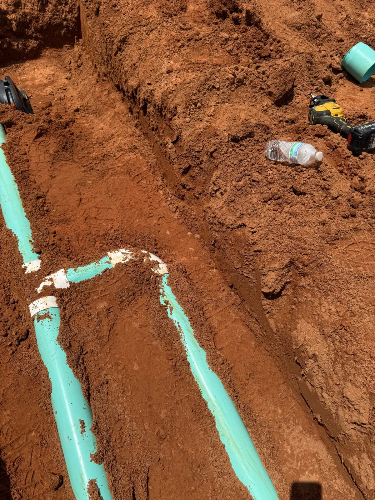 Teal pipe run laid in a red-clay trench